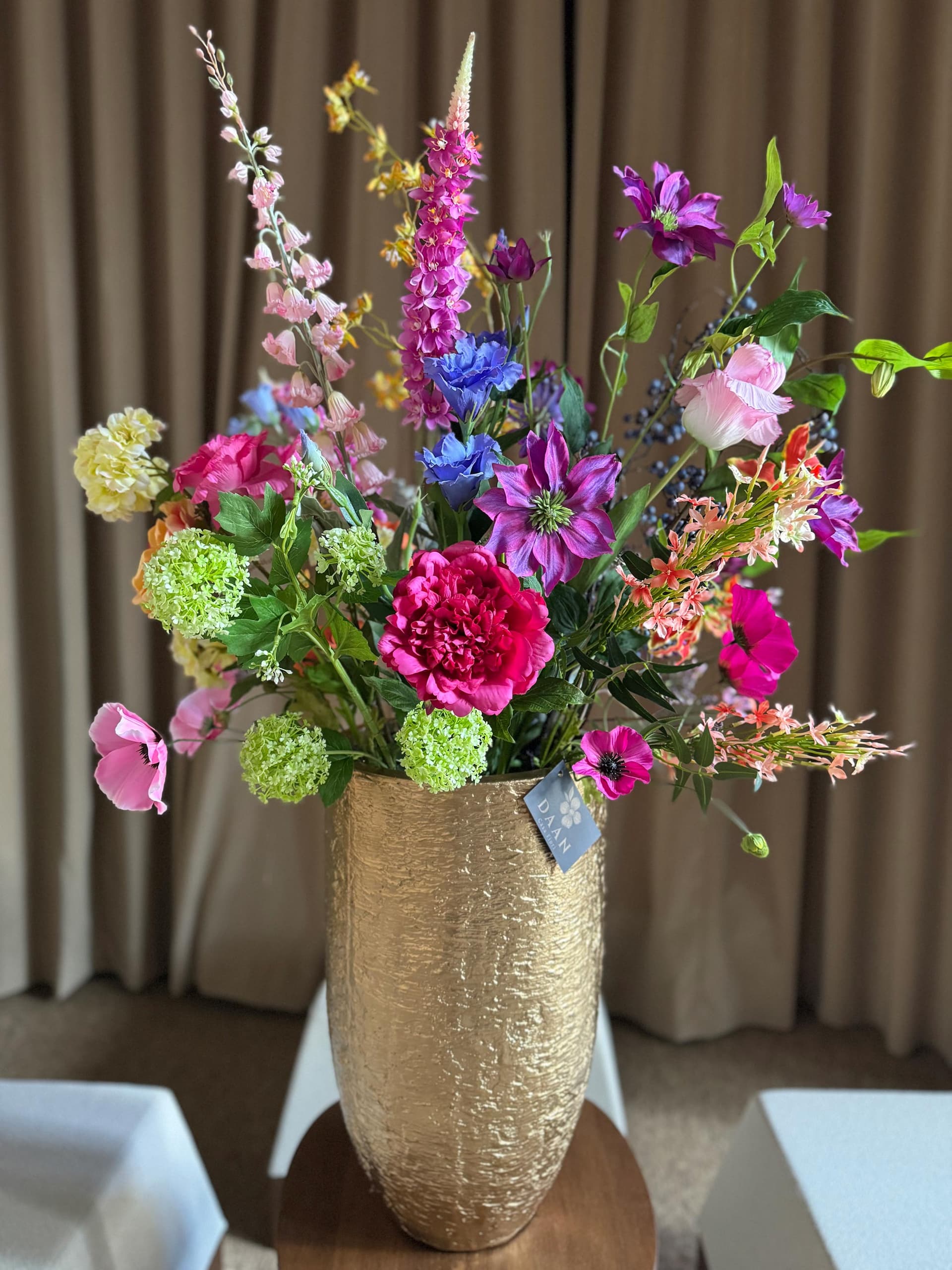Hoge gouden vaas met structuur en roze, paarse en blauwe zijden bloemen voor gordijnen
